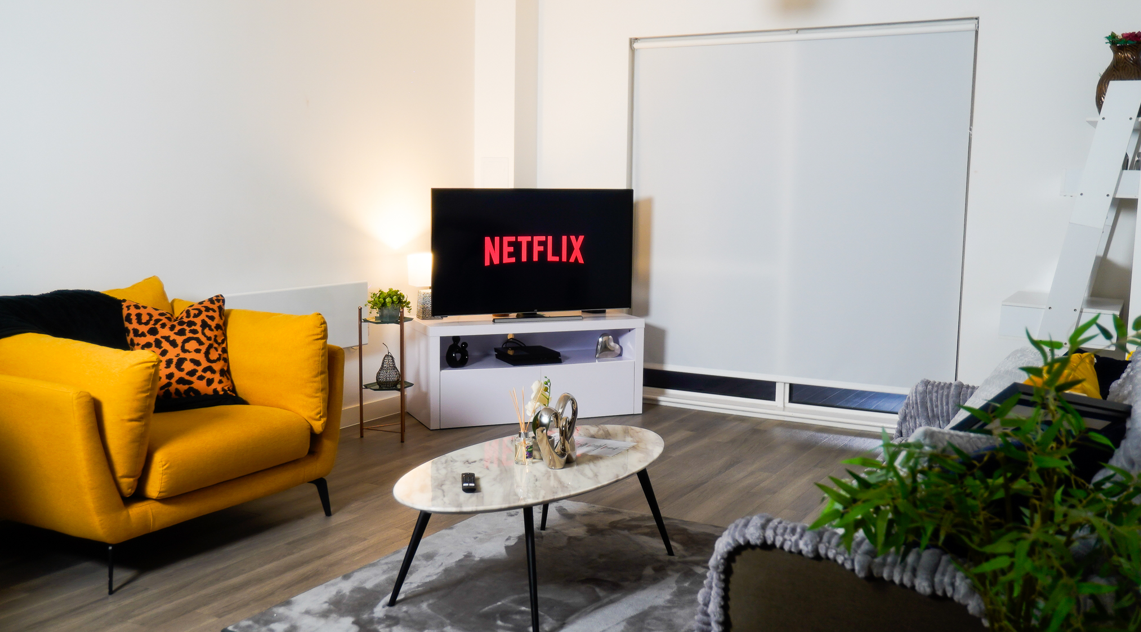 Modern living room with bright yellow sofa, marble coffee table, entertainment system, and large windows with natural light